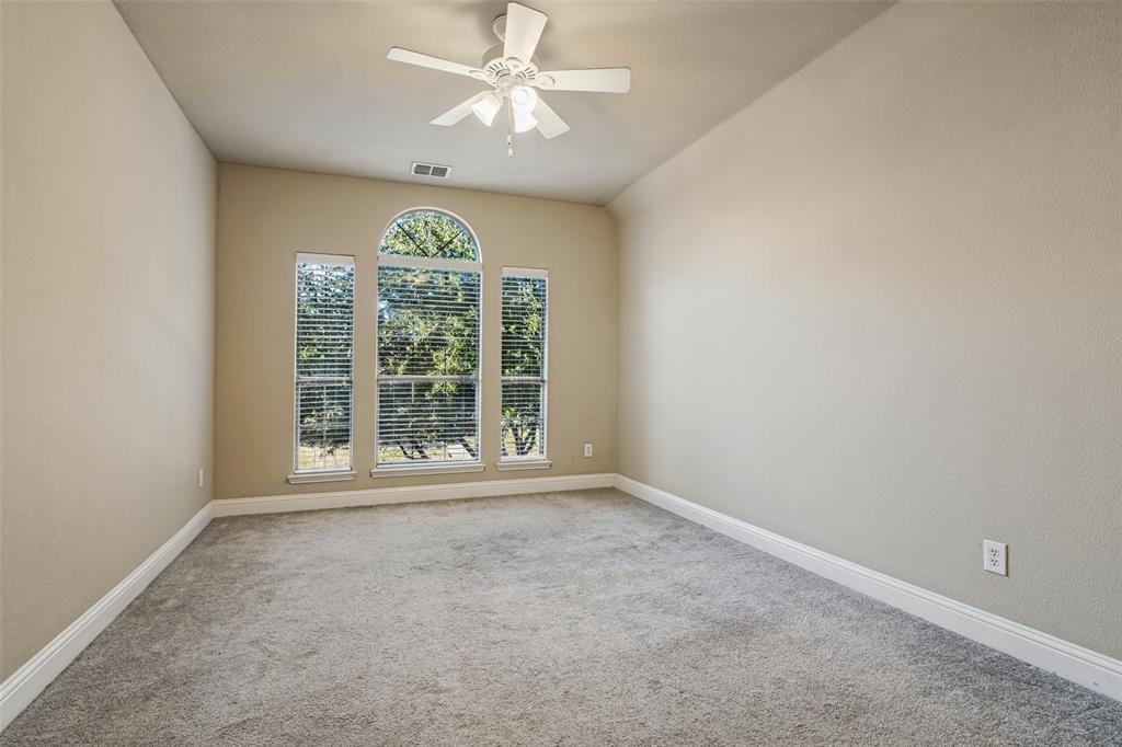 Neutral-toned interior featuring carpeting, a centrally located ceiling fan with integrated lighting, and a set of windows including a central arched window