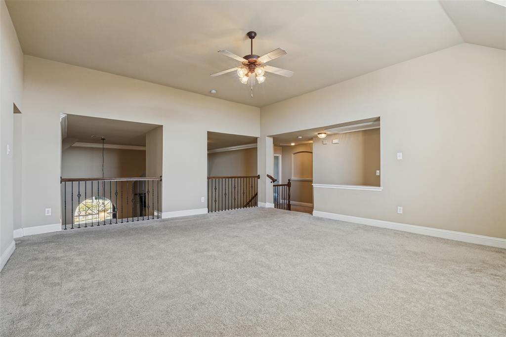 Vaulted ceiling featuring a central ceiling fan with multi-light fixture, carpeted flooring, and decorative metal baluster railings