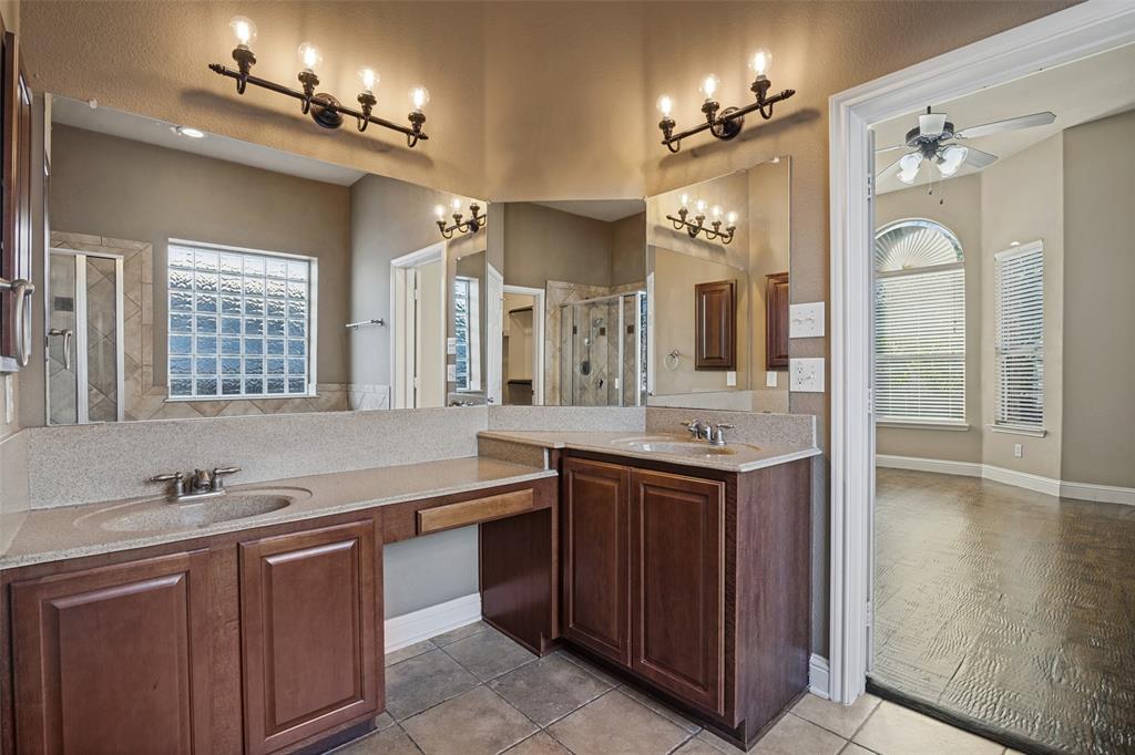 Dual-vanity bathroom featuring raised-panel wood cabinetry, stone-composite countertops, multi-light vanity fixtures, and tiled flooring