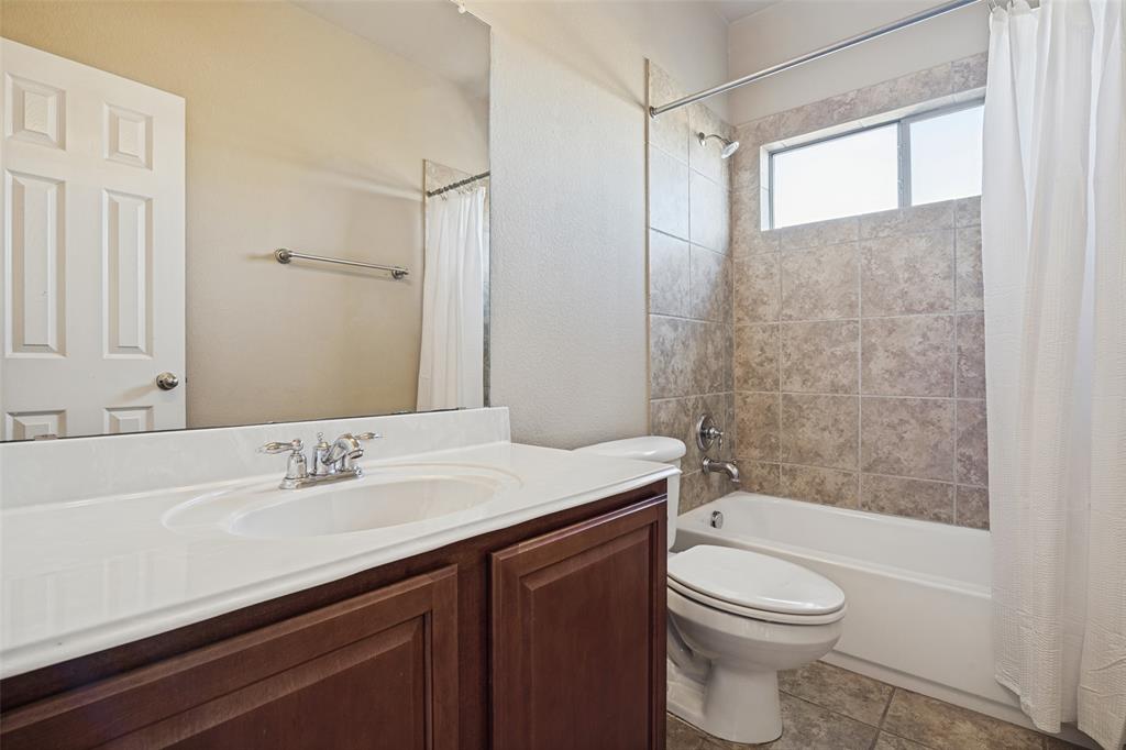 Bathroom featuring a dark wood-finish vanity with a white countertop, inset sink, polished metal faucet, full-width wall mirror, and a tub-shower combination with tile surround