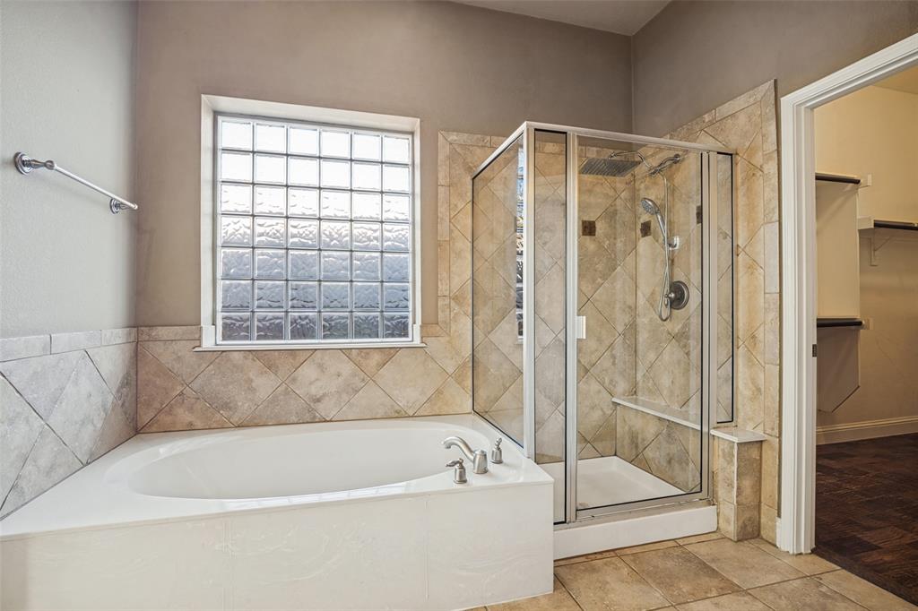 Bathroom featuring a drop-in soaking tub, a glass-enclosed shower with a rainfall showerhead, diamond-patterned wall tile, and a glass block window