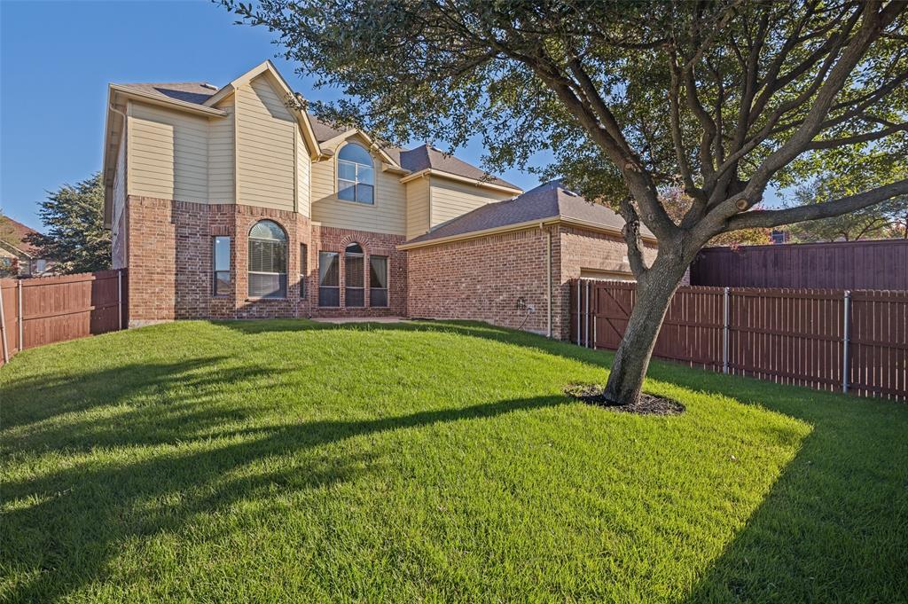 Rear exterior featuring a brick and siding facade, arched windows, and a fenced backyard with a mature tree