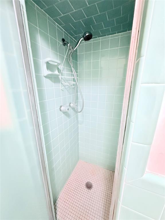 Shower stall featuring square ceramic wall tiling, ceiling tile finish, handheld showerhead, and integrated soap dish