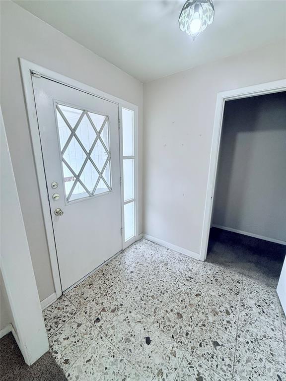 Entryway featuring diamond-pattern glass door inlay, vertical side-light window, and large-format aggregate flooring