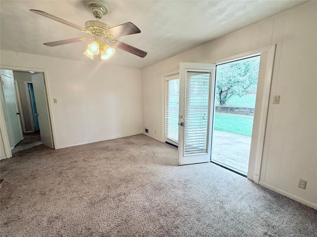 Interior space featuring carpeting, a ceiling fan with integrated lighting, paneled walls, and a glass-paneled door providing access to a concrete patio