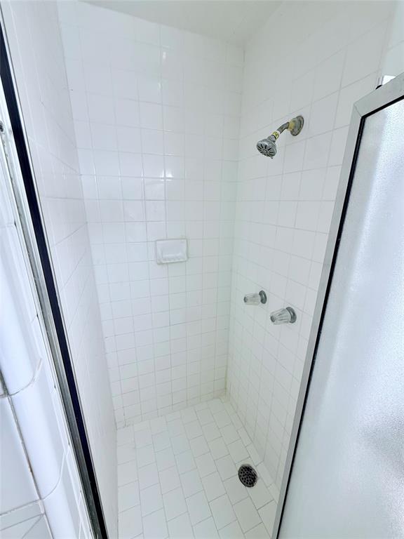 Shower stall featuring white square wall tile, white rectangular floor tile, integrated recessed soap niche, and metal hardware
