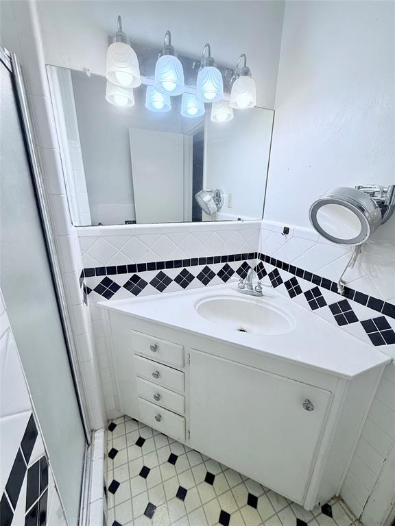 Corner vanity featuring white cabinetry, a molded sink, diamond-pattern tile backsplash, and a multi-light fixture with glass shades