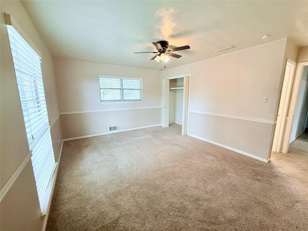 Room featuring neutral-toned walls with horizontal chair rail molding, wall-to-wall carpeting, ceiling fan with integrated lighting, and a closet with sliding doors