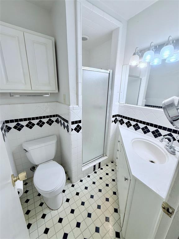 Bathroom featuring a corner vanity with integrated sink, shower enclosure with frosted glass door, wall-mounted cabinetry, geometric tile flooring, and decorative diamond-pattern wall tile accents