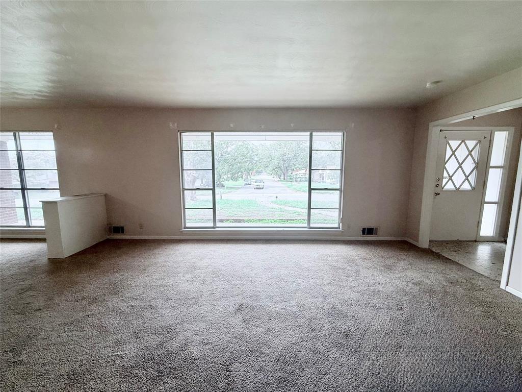 Spacious room featuring a large picture window, wall-to-wall carpeting, and an entry door with diamond-patterned glass inlay