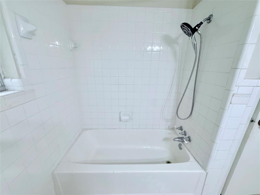 Built-in white porcelain tub with square tile surround, chrome hand-held shower fixture, and recessed soap dish