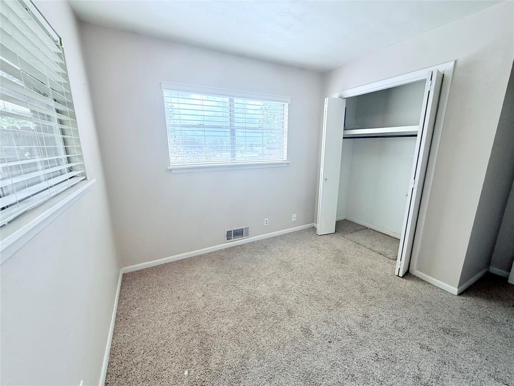 Neutral-toned room featuring neutral carpeting, white walls, horizontal window blinds, and a built-in closet with folding doors