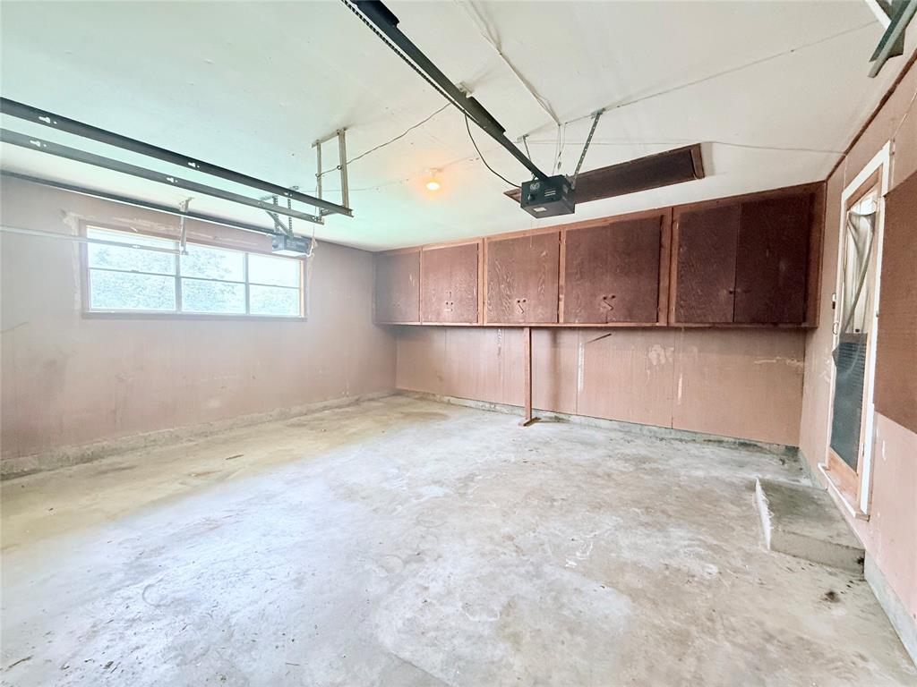 Multi-car garage featuring concrete flooring, built-in wooden cabinetry, a multi-pane window, and an integrated garage door opener system