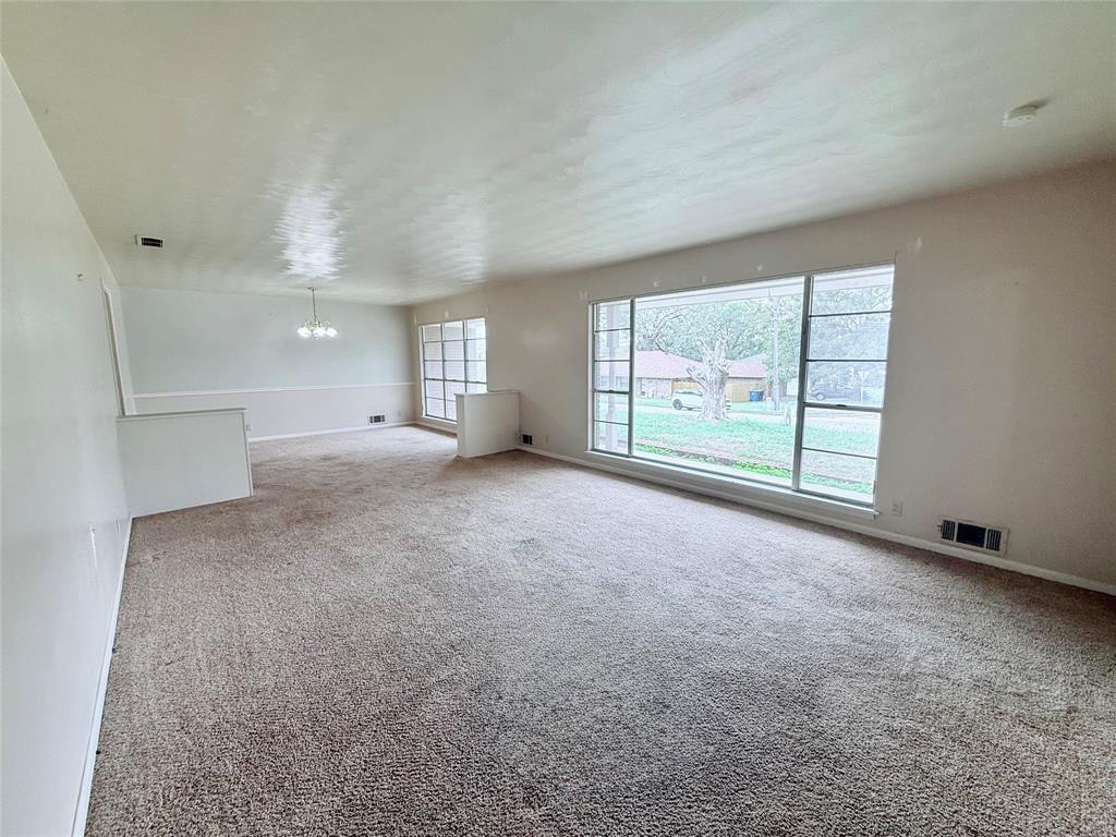 Spacious interior featuring neutral carpeting, a large picture window, multi-pane accent windows, chair rail molding, and a tiered architectural half-wall
