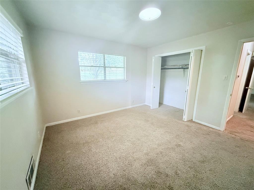 Neutral wall color, carpeted flooring, dual-pane windows with horizontal blinds, ceiling-mounted light fixture, and closet with sliding doors