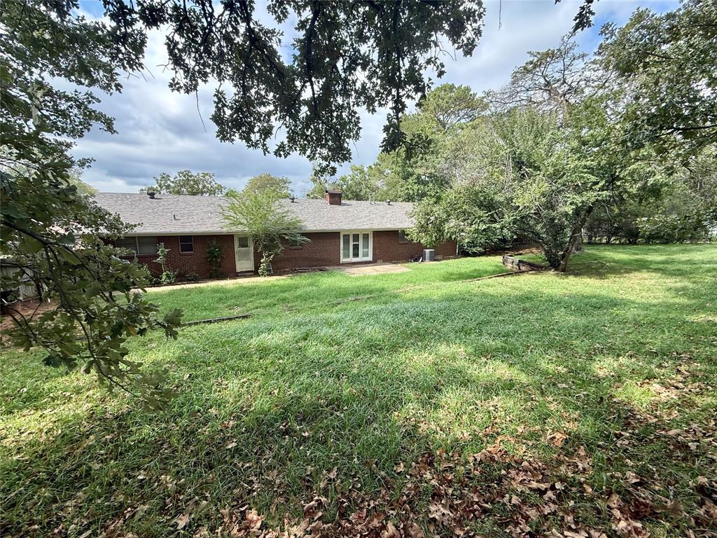Exterior elevation featuring a red brick facade, asphalt shingle roof, expansive backyard, and mature trees