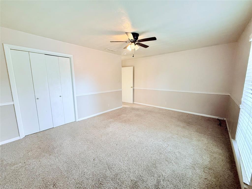 Interior space featuring carpeted flooring, two-paneled closet doors, a central ceiling fan with integrated lighting, and chair rail molding