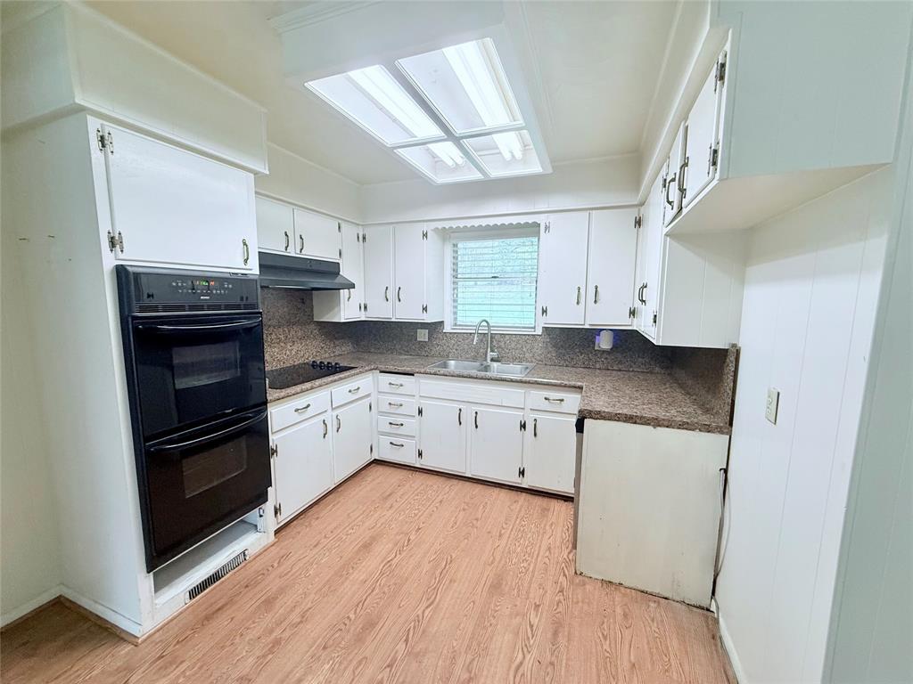 Kitchen featuring white cabinetry, wood-finish flooring, a built-in double oven, stone-patterned countertops, and a recessed skylight