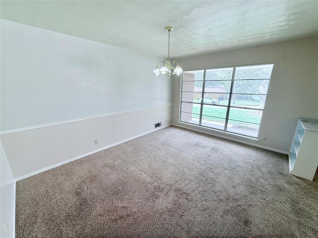 Interior space featuring neutral wall-to-wall carpeting, chair rail molding, a large multi-pane window, and a multi-arm chandelier