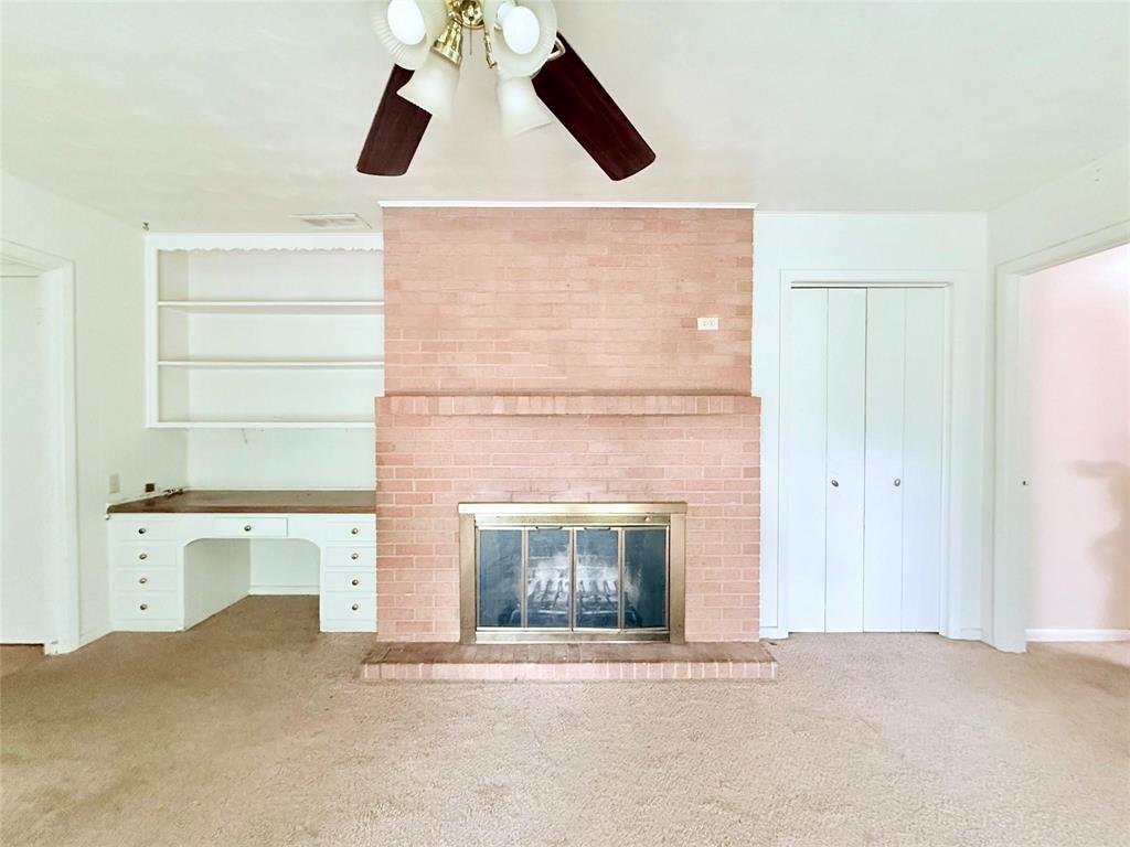 Brick fireplace with a metal screen and hearth, built-in desk with drawers, open wall shelving, and a ceiling-mounted light fixture