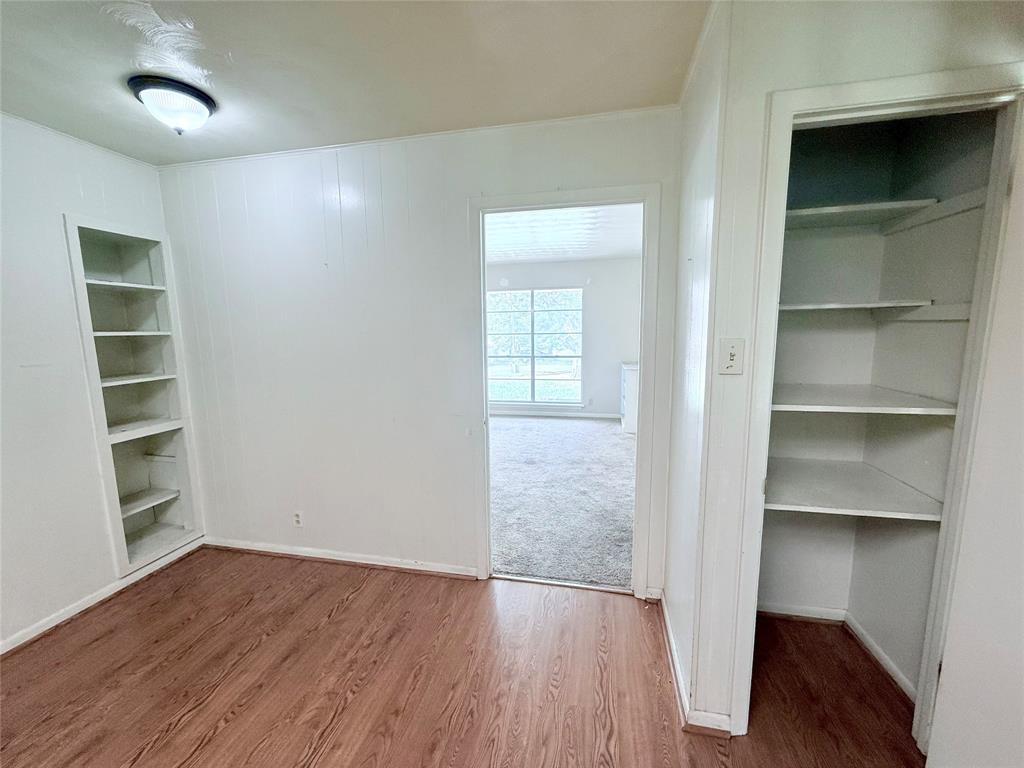 Room interior featuring wood-finish flooring, built-in wall shelving, a flush-mount light fixture, and an open closet with built-in storage shelves