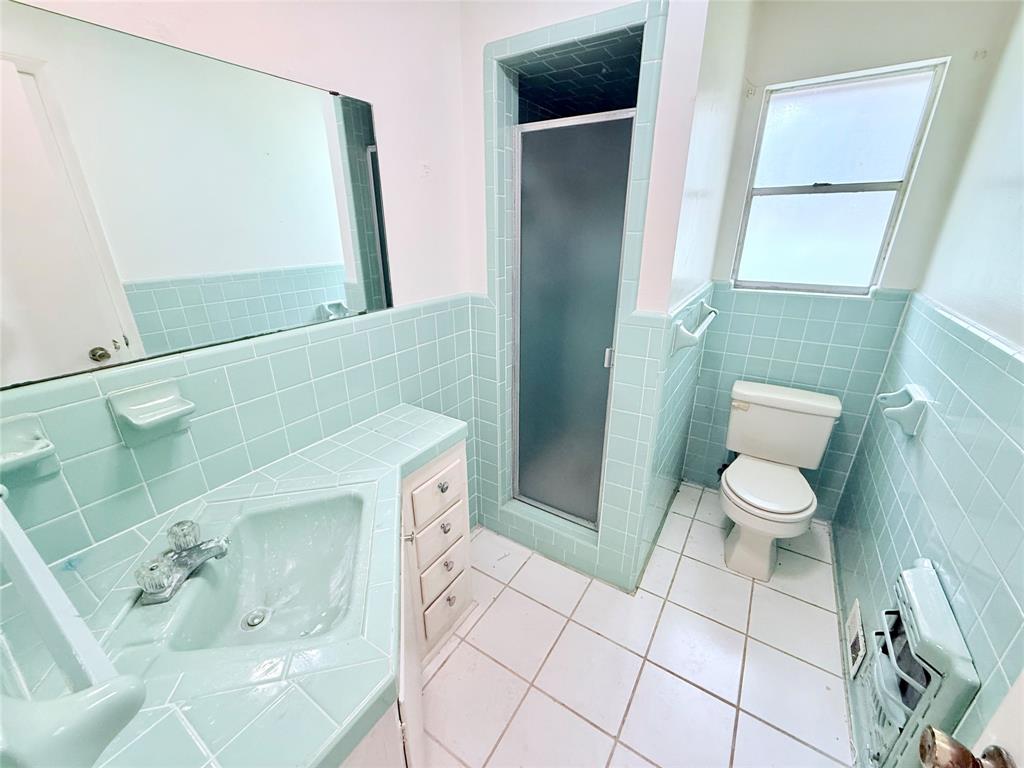 Bathroom featuring square ceramic wall tiling, a vanity with a tiled countertop and integrated sink, a walk-in shower enclosure with a frosted door, and white floor tile