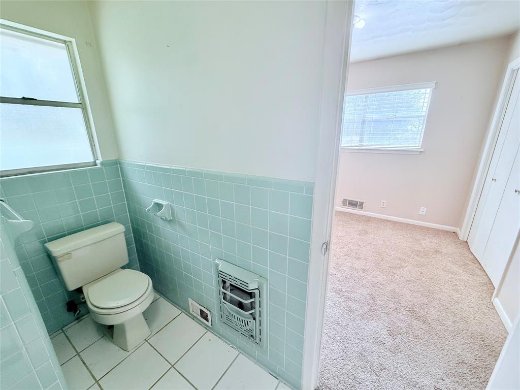 Bathroom featuring light blue wall tiles, white floor tile, a porcelain toilet, and a built-in wall heater