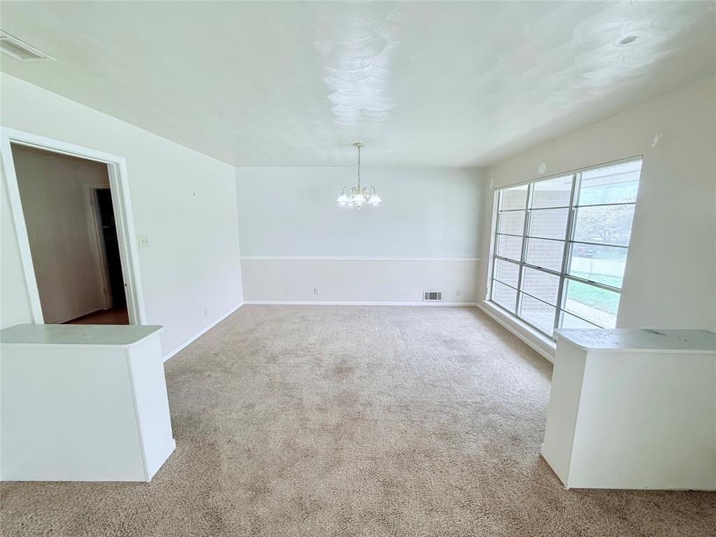 Large room featuring carpeted flooring, white wainscoting, a multi-light chandelier, and a substantial window pane assembly