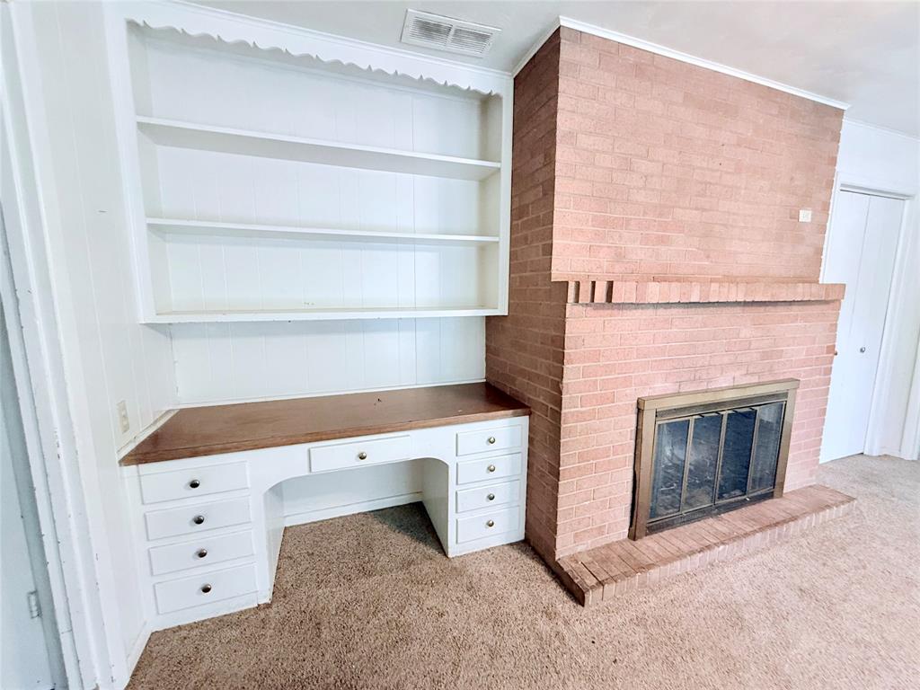 Brick fireplace surround with a raised hearth, metal fireplace screen, and integrated white built-in desk with multiple drawers and open shelving