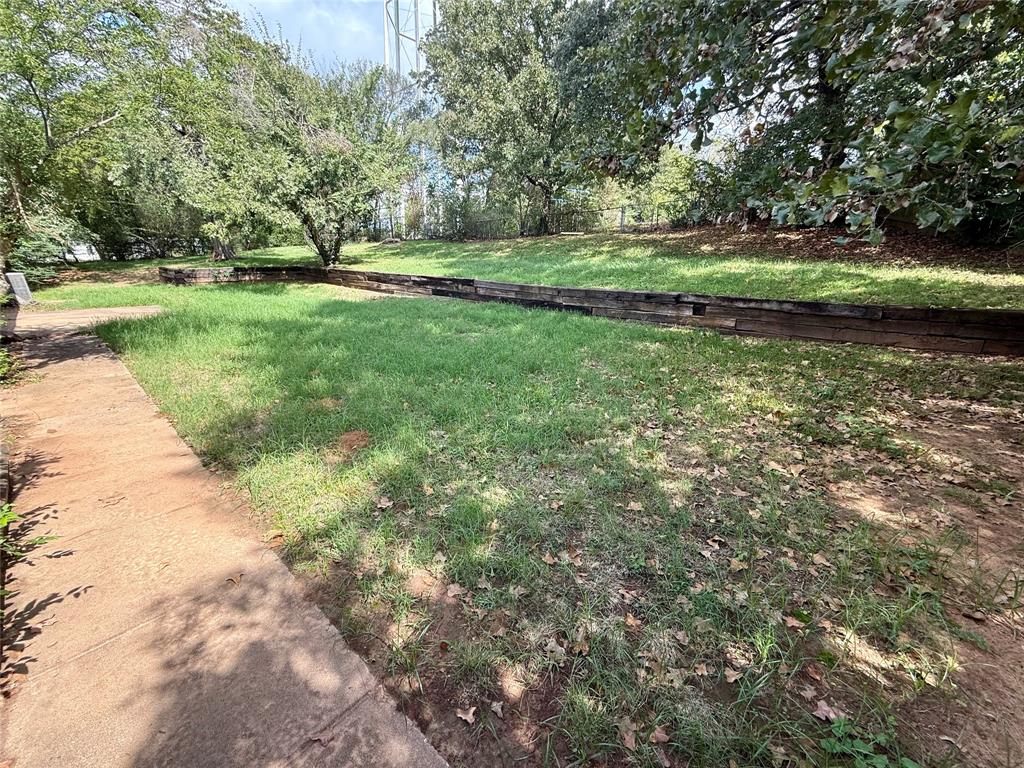 Rear yard featuring a concrete path, tiered landscape retaining walls, grass lawn, and mature trees