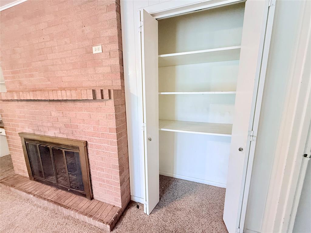 Floor-to-ceiling brick fireplace with a metal firebox and mantel, accompanied by a built-in storage closet featuring shelving and bifold doors