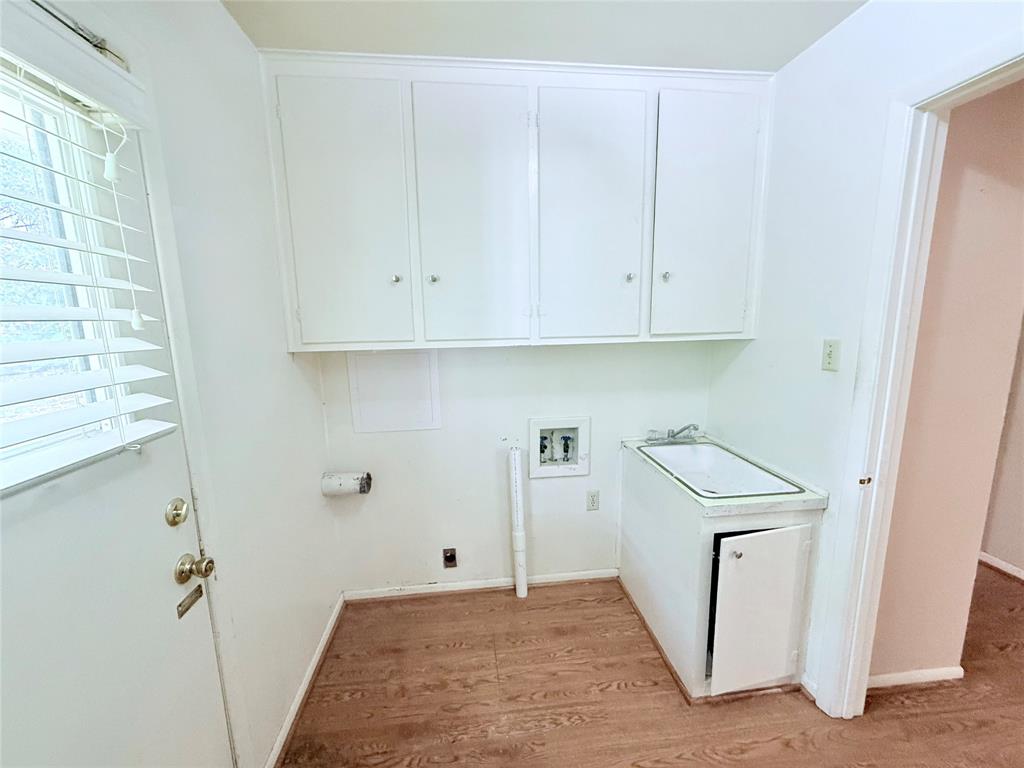 Utility room featuring wood-finish flooring, white wall-mounted cabinetry, a built-in basin sink with cabinet storage, and exterior door access