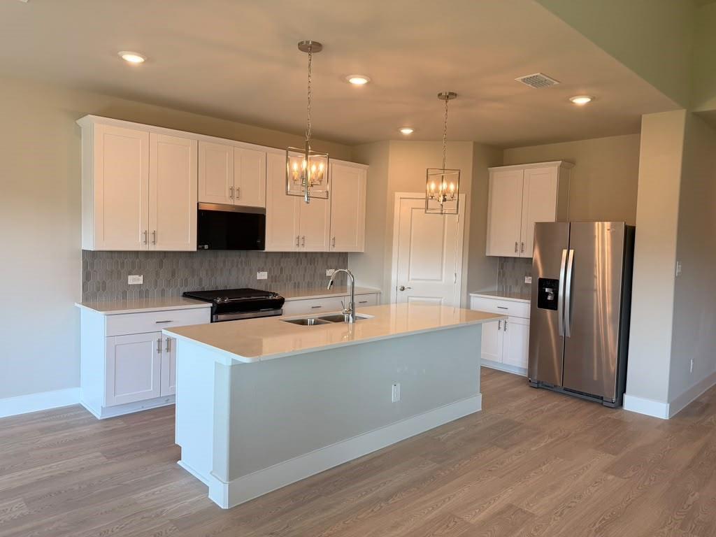 Kitchen featuring white shaker-style cabinetry, quartz countertops, a central island with a double-basin sink, geometric pendant lighting, and wood-finish flooring