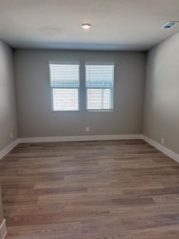 Interior room featuring neutral-toned wall paint, wood-finish flooring, and two windows with horizontal blinds