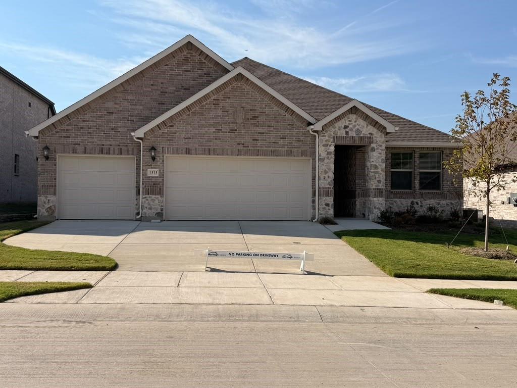 Brick and stone exterior featuring a gabled roofline, three-car garage, and concrete driveway Brick and stone exterior featuring a gabled roofline, three-car garage, and concrete driveway