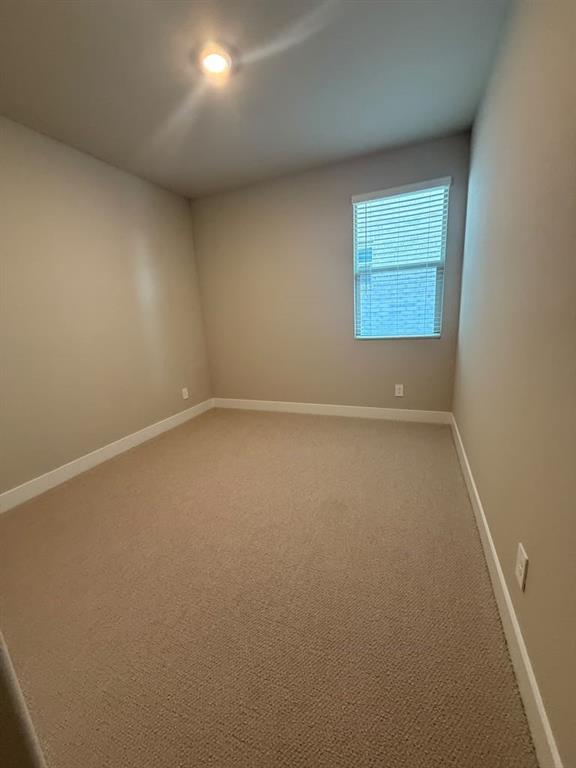 Neutral-toned interior space featuring wall-to-wall carpeting, a single window with horizontal blinds, and a flush-mount ceiling light fixture