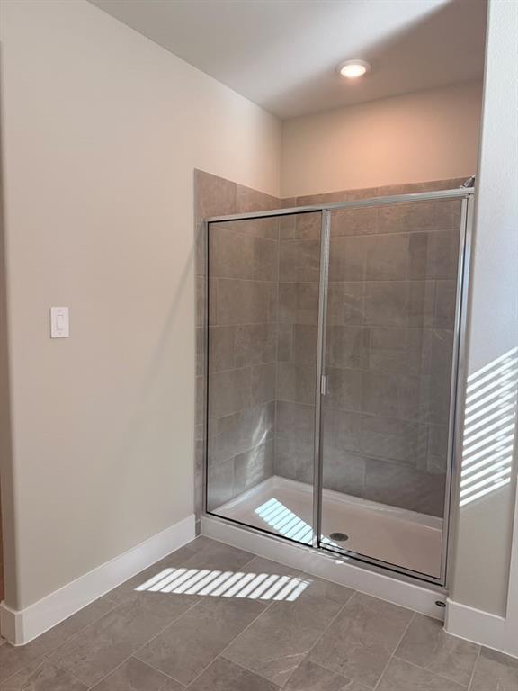 Walk-in shower featuring a sliding glass door, neutral-toned tiled surround, and matching tiled flooring
