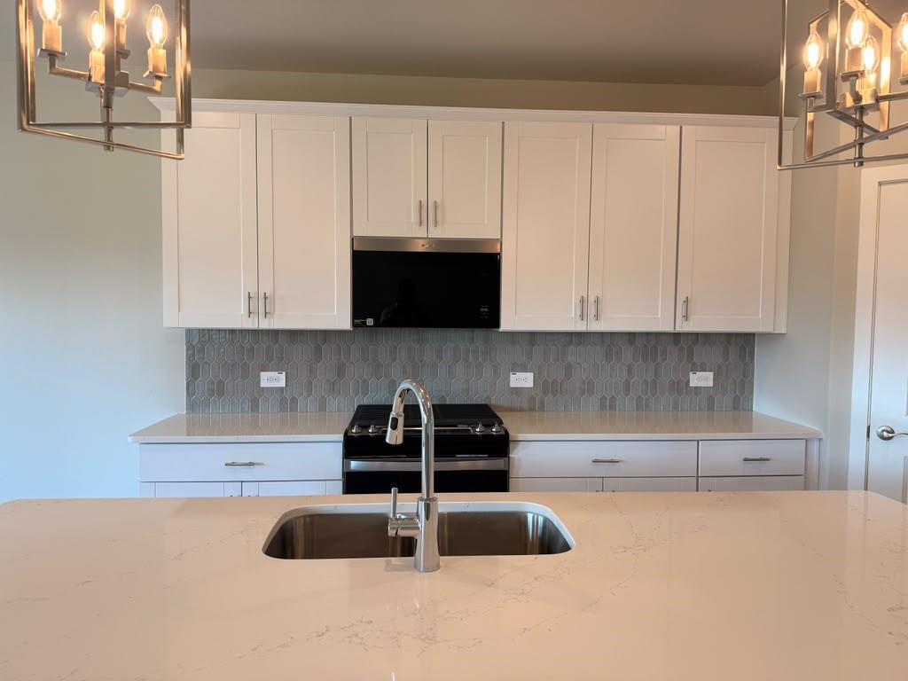 Kitchen featuring white shaker-style cabinetry, quartz countertops, a patterned tile backsplash, stainless steel undermount sink with a gooseneck faucet, and two industrial-style pendant light fixtures