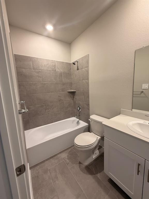 Bathroom featuring a white bathtub, grey tile wall surround, grey floor tiling, vanity with a solid-surface countertop, and a built-in mirror