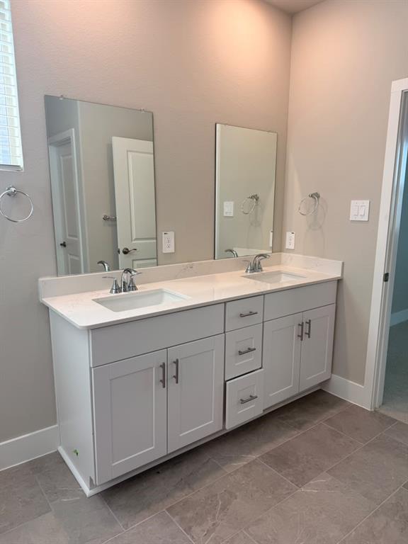 Double-sink vanity featuring white shaker-style cabinetry, stone-composite countertop with integrated rectangular basins, polished chrome fixtures, and dual frameless mirrors
