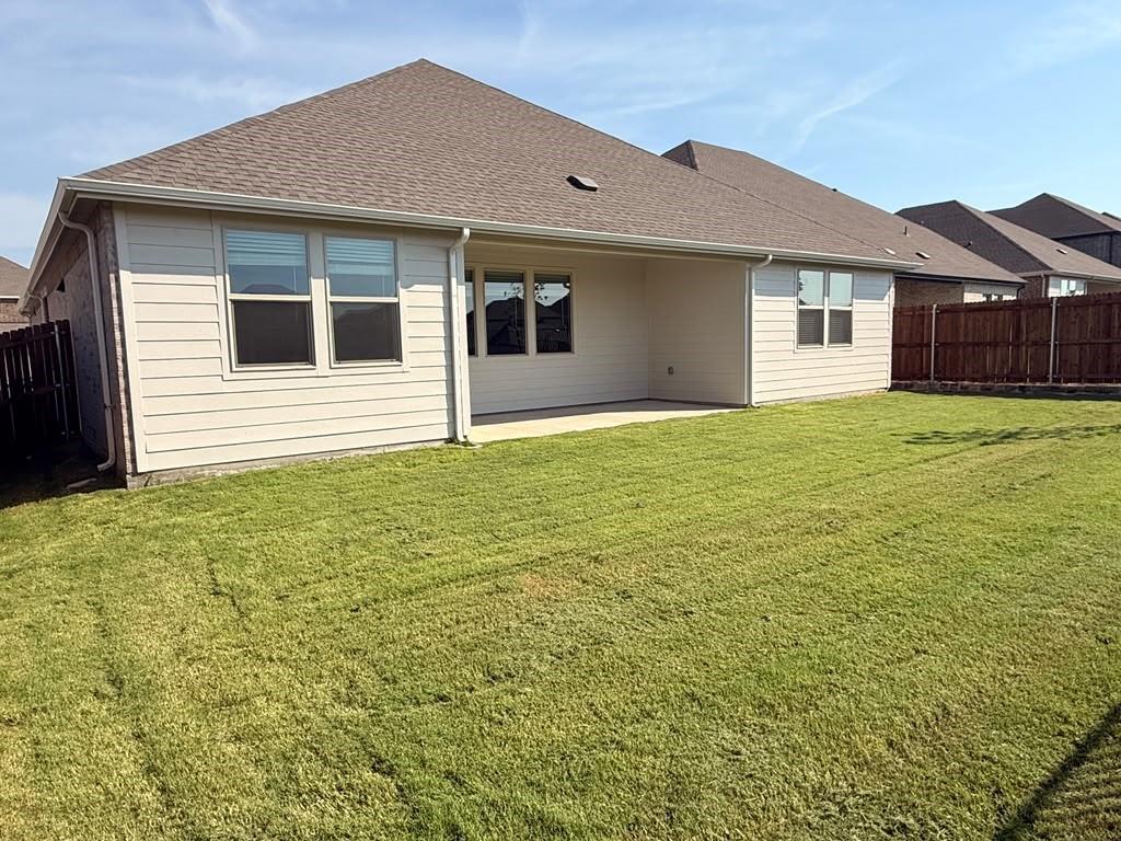 Rear exterior featuring horizontal lap siding, a covered concrete patio, multi-pane windows, asphalt shingle roofing, and a privacy-fenced backyard