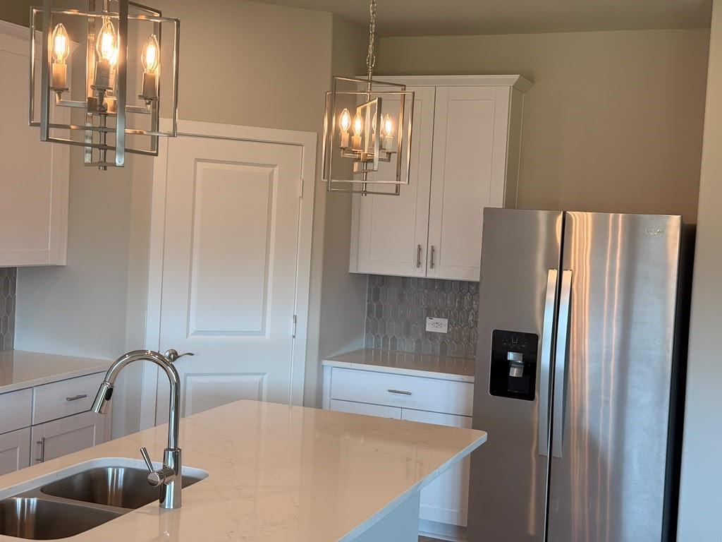 Kitchen featuring white cabinetry, solid surface island countertop, stainless steel refrigerator, geometric pendant lighting, and a neutral-toned tile backsplash