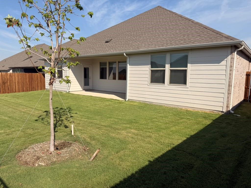 Rear exterior featuring horizontal lap siding, a concrete patio, a shingled roof, and a fenced backyard with a lawn