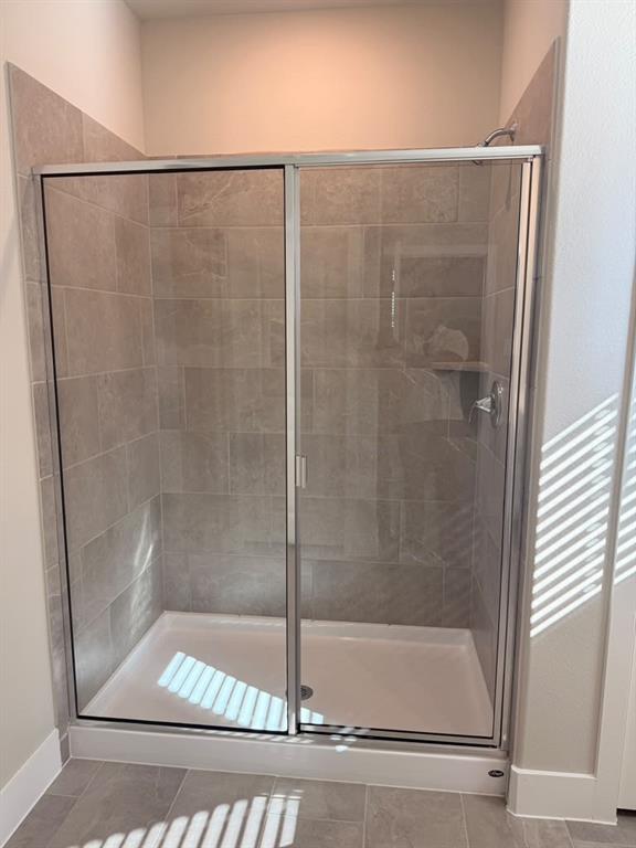 Walk-in shower featuring a chrome-framed glass sliding door, neutral-toned tile surround, and a low-profile white shower base