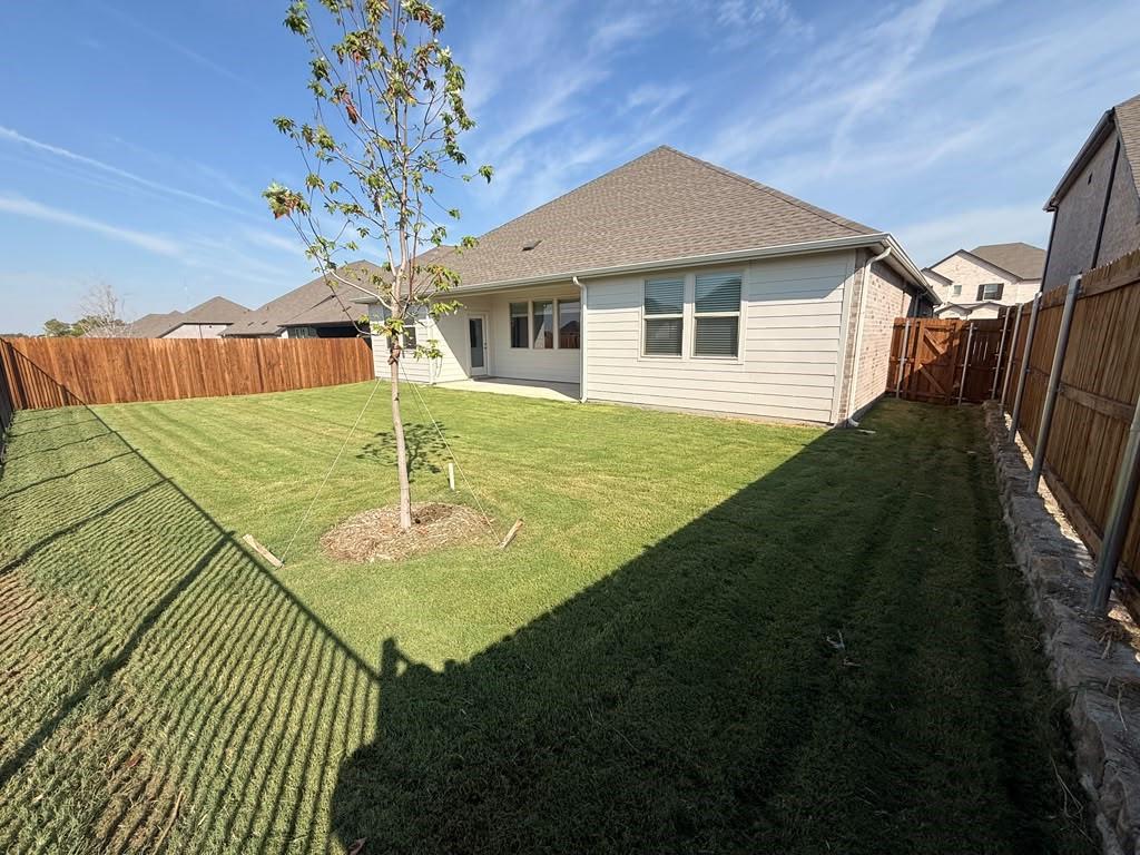 Private fenced backyard featuring a grass lawn, stone retaining wall, and horizontal wood-style fencing