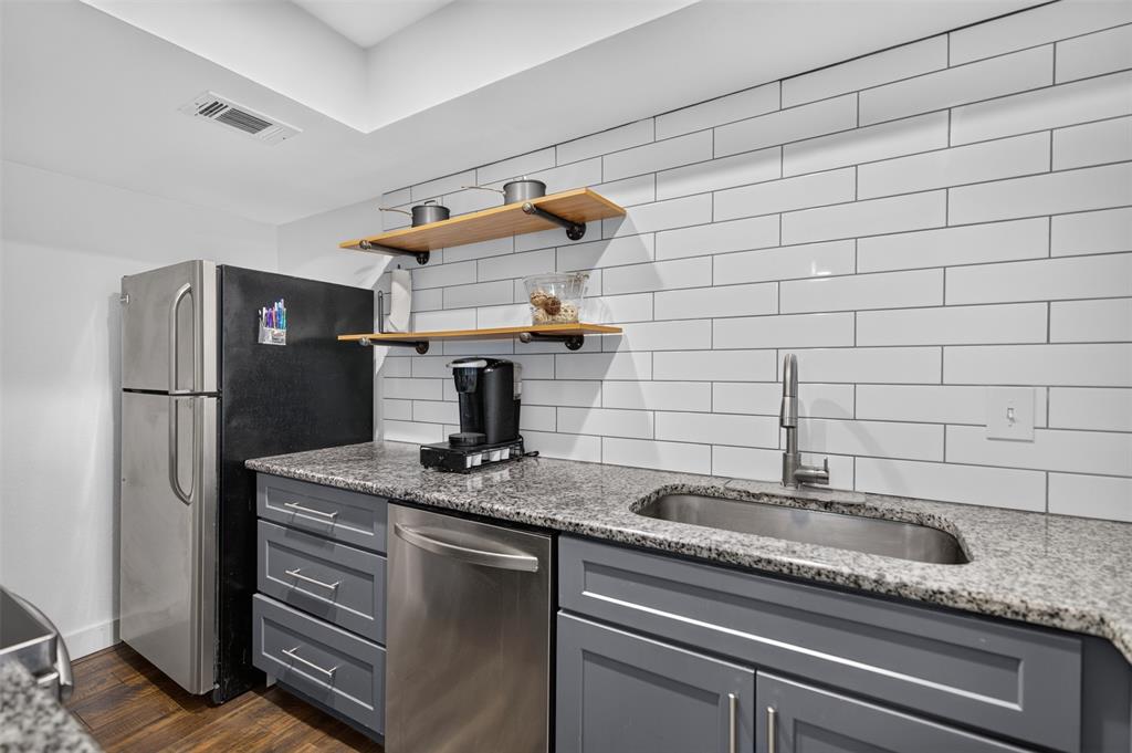 Kitchen featuring stone-finish countertops, subway tile backsplash, shaker-style cabinetry, stainless steel dishwasher, and built-in wood shelving