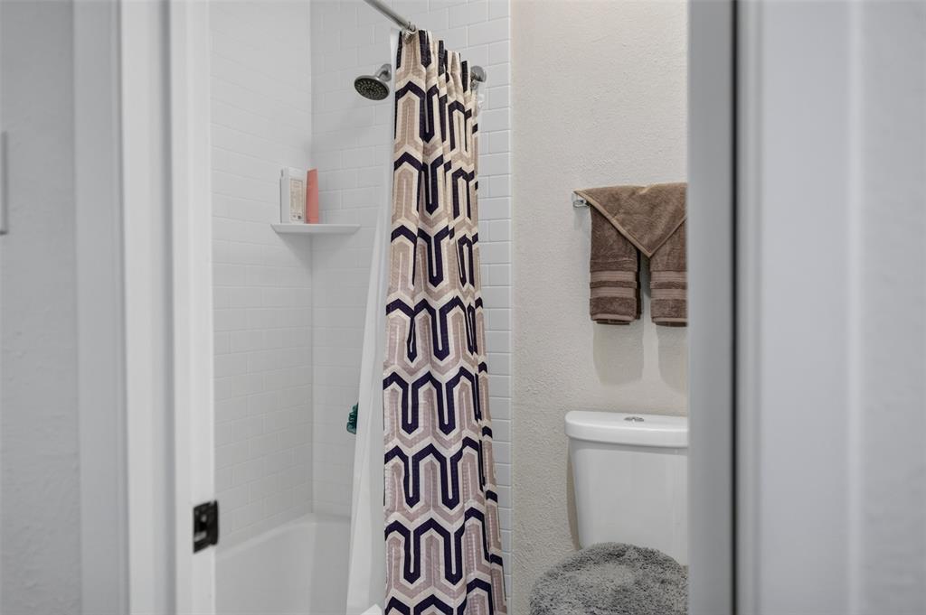 Full bathroom featuring white subway tile shower surround, integrated corner shelf, wall-mounted towel bar, and standard-height toilet