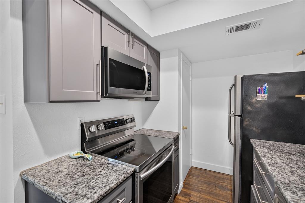 Kitchen featuring stone-finish countertops, subway tile backsplash, shaker-style cabinetry, stainless steel dishwasher, and built-in wood shelving