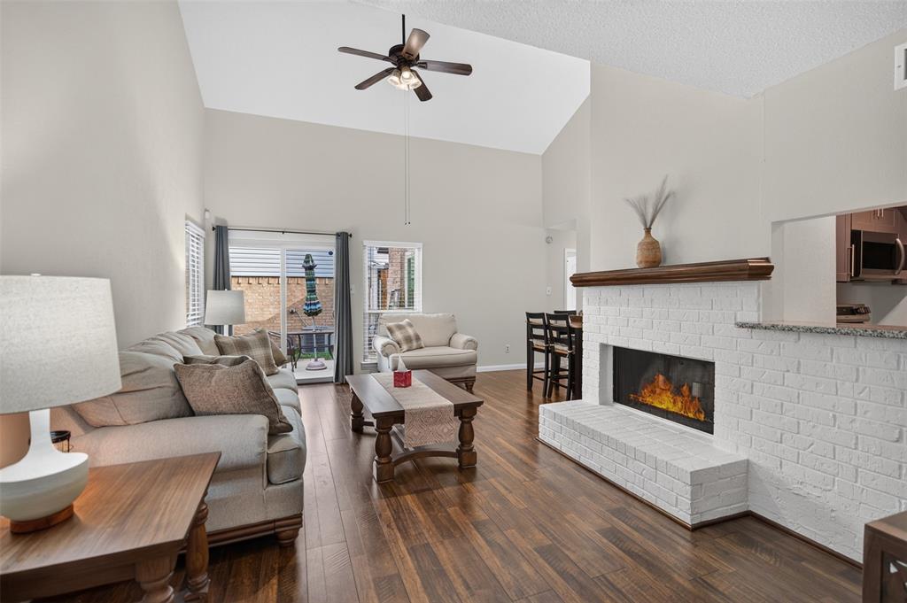 Vaulted ceilings, wood-finish flooring, white painted brick fireplace with a wood mantel, ceiling fan, and sliding glass door leading to an outdoor space