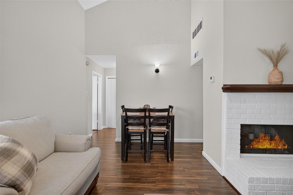 Living area featuring double-height ceilings, wood-finish flooring, and a white brick fireplace with a wood mantel